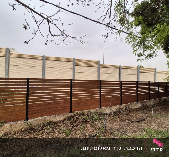 גדר עץ עם עמודי מתכת ברקע קיר בטון